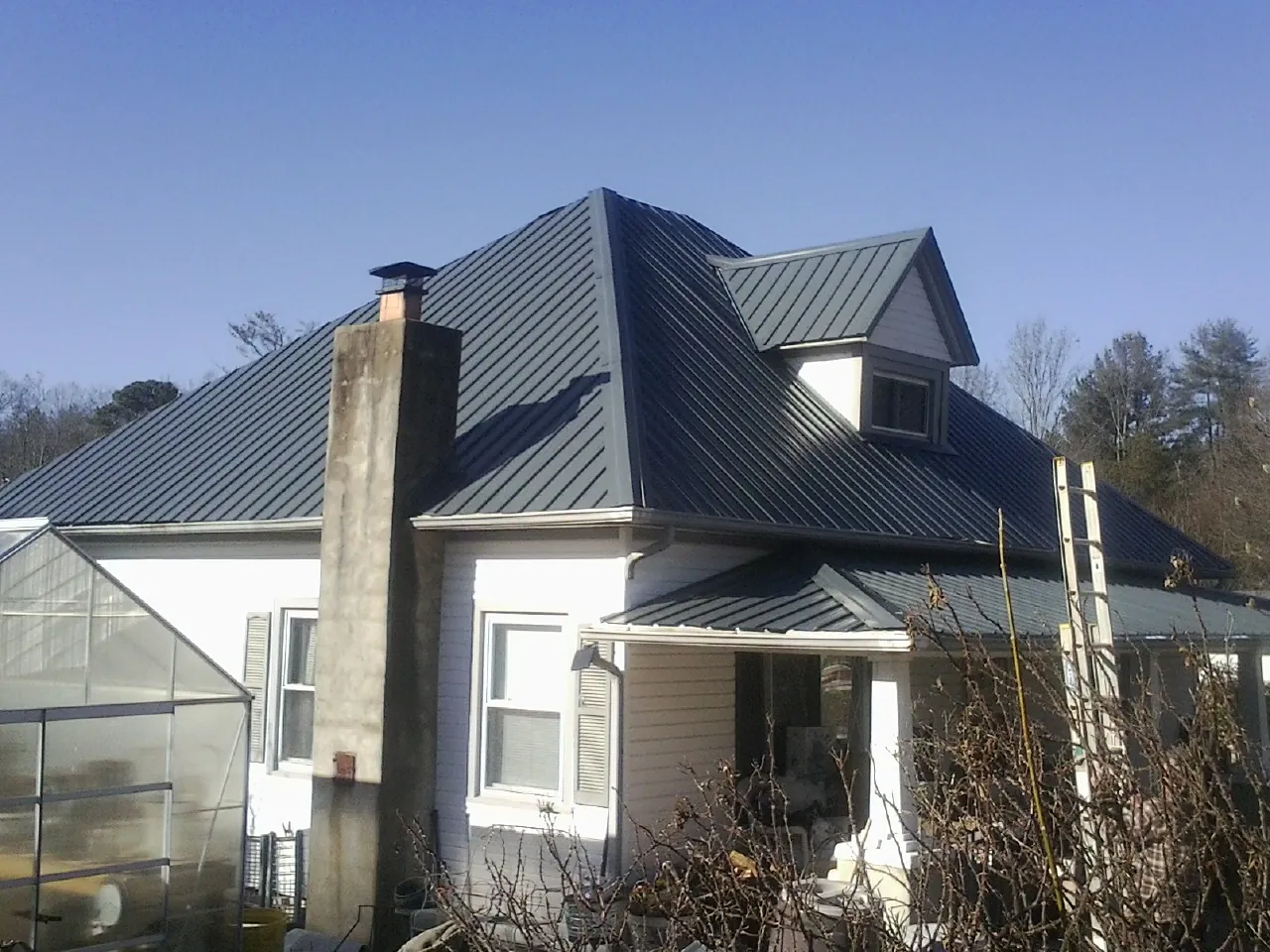 Dark blue standing seam metal roof on a white farmhouse with dormer — Slate & Tile Roof Repair by Roofing Brothers in Williamson