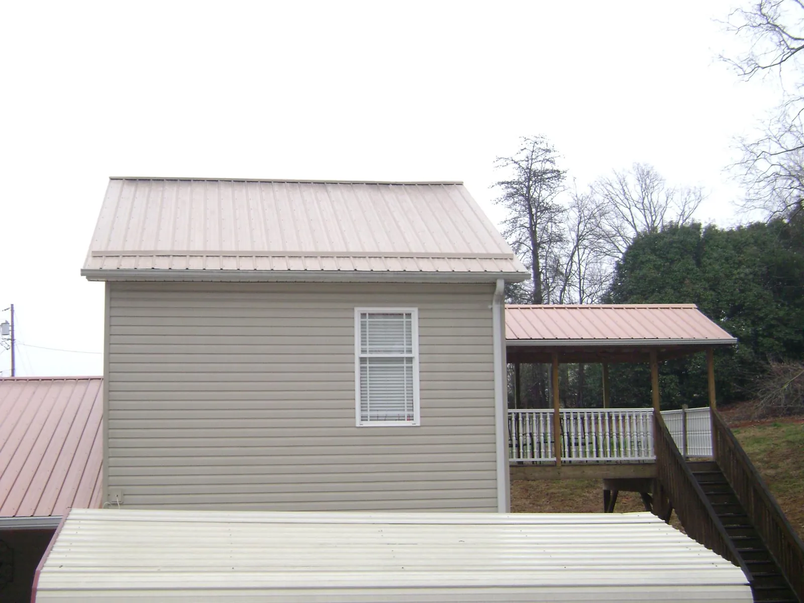 Tan metal roofs on a two story addition and attached porch, from a Roof Replacement job in Williamson